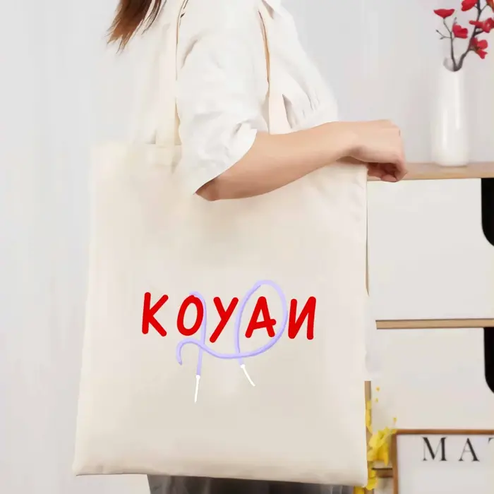 Un sac fourre-tout en toile de couleur crème avec texte Koyani et motifs de motifs abstraits pour un